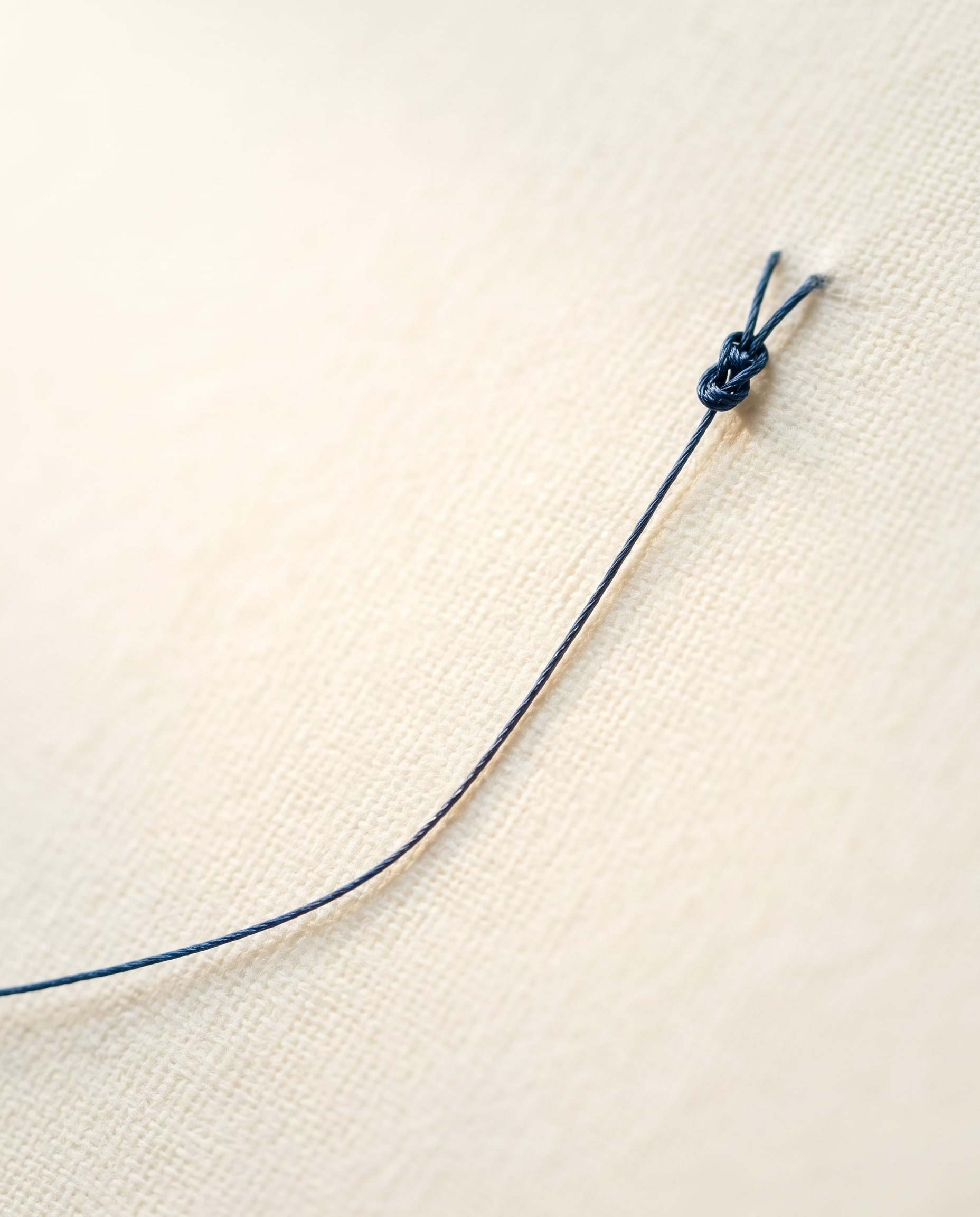 Macro study of fine suture thread crossing a softly lit, textured surface.